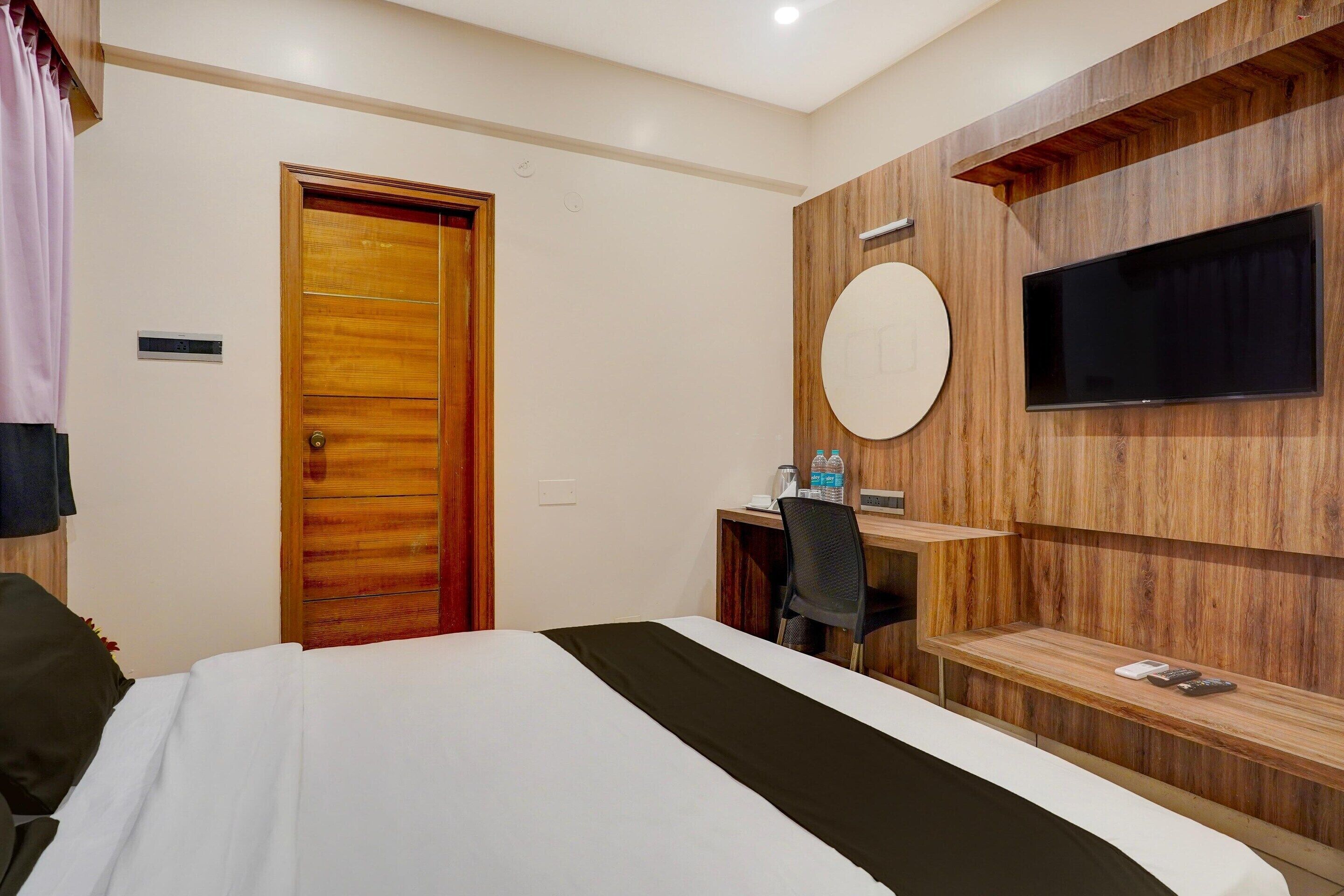 A hotel room with a bed, a desk, a chair, a television mounted on the wall, and a wooden door.