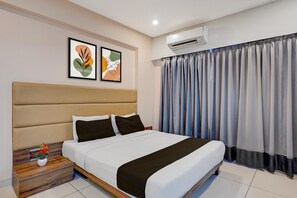 Une chambre d’hôtel moderne avec un grand lit, une table de chevet en bois, un climatiseur fixé au mur et une fenêtre avec des rideaux.