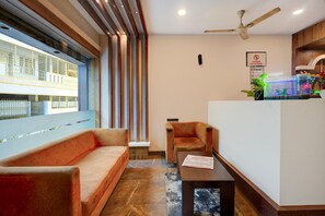 Un hall d’hôtel avec un canapé, un fauteuil, un comptoir d’accueil et un ventilateur de plafond.