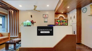 A reception area with a sign reading 'Townhouse Company-Serviced,' a reception desk, a clock, and a staircase leading to an upper floor. - Deluxe Silver Key Hotel (Bengaluru)