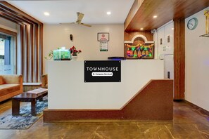Een receptiegedeelte met een bord waarop 'Townhouse Company-Serviced' staat, een receptiebalie, een klok en een trap die naar een verdieping leidt.