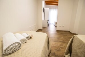 A hotel room with a bed, two rolled towels, a wooden floor, and a view into the bathroom. - Quattro Canti (Carini)