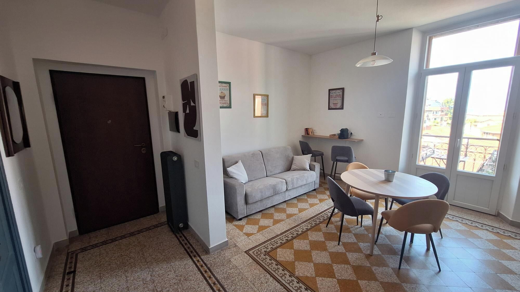 Una sala de estar con sofá, una mesa de comedor con sillas, un ventanal grande y una puerta.