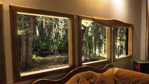 A room with a bed, two large windows with a forest view, and a wooden headboard.