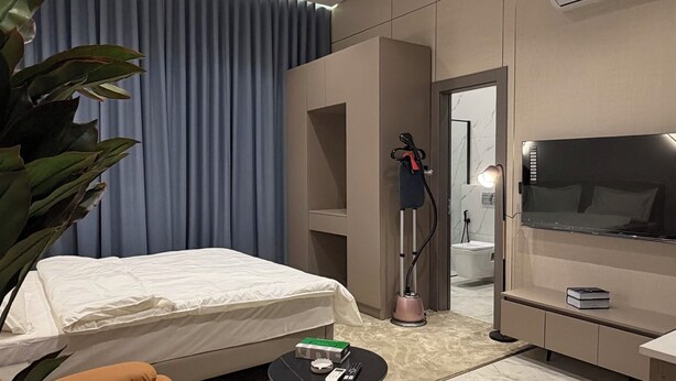 Ein modernes Hotelzimmer mit Bett, Schreibtisch, Stuhl, einer Topfpflanze und einer Deckeninstallation.