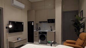 Ein modernes Schlafzimmer mit einem großen Bett, einem an der Wand montierten Fernseher, einer integrierten Waschmaschine und einem Trockner sowie einer kleinen Küchenzeile.