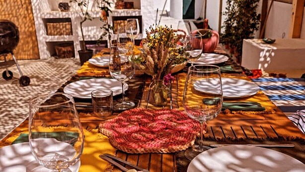 An outdoor dining area with a table set for a meal, surrounded by plants and a wooden fence. - Duck House (Comporta)