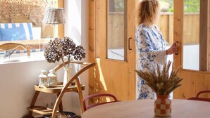 A wooden interior with a dining table, chairs, a hanging light fixture, and a view through a door. - Duck House (Comporta)