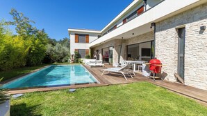 A modern house with a swimming pool, outdoor seating, and a barbecue area.
