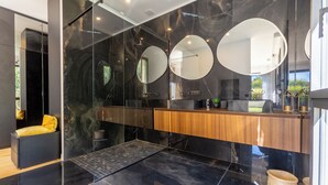 A modern bathroom with a glass shower enclosure, a wooden vanity, and three round mirrors.