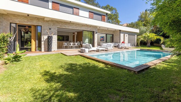 A modern two-story house with a swimming pool, outdoor seating, and a well-maintained lawn.