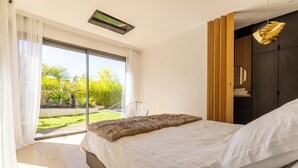 A modern bedroom with a large bed, a view of a garden, and a ceiling fan.