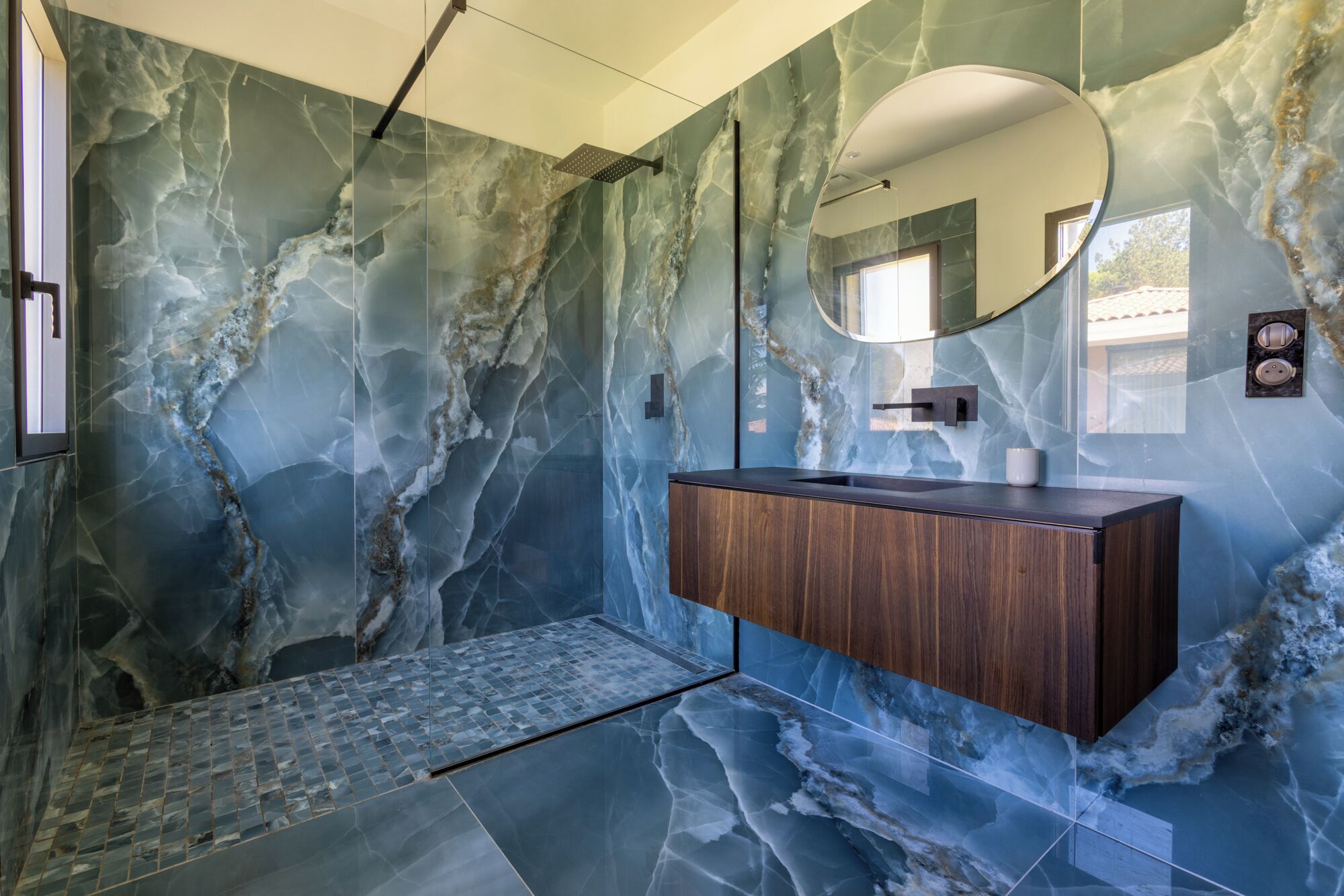 Une salle de bain avec des murs en marbre, un meuble-lavabo en bois, un grand miroir et un espace douche.