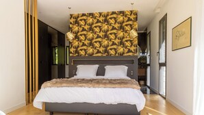 A modern bedroom with a large bed, a dark headboard, and a tropical leaf-patterned wallpaper.