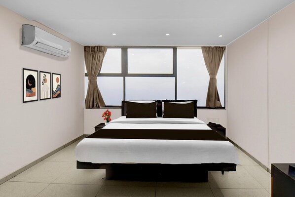 Habitación de hotel con una cama grande, aire acondicionado, ventana con cortinas y cuadros en la pared.