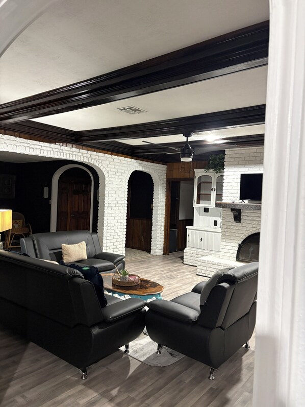 A living room with a fireplace, black leather sofas, and a wooden floor.
