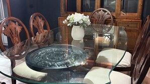Ein Essbereich mit Tischplatte aus Glas, Holzstühlen, einer Vase mit Blumen und einem Schrank mit Glastüren.