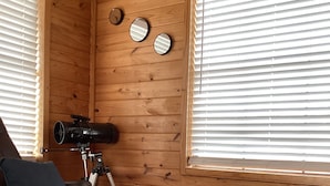L’intérieur d’un chalet en bois, avec un canapé en cuir, un télescope et une fenêtre équipée de stores.