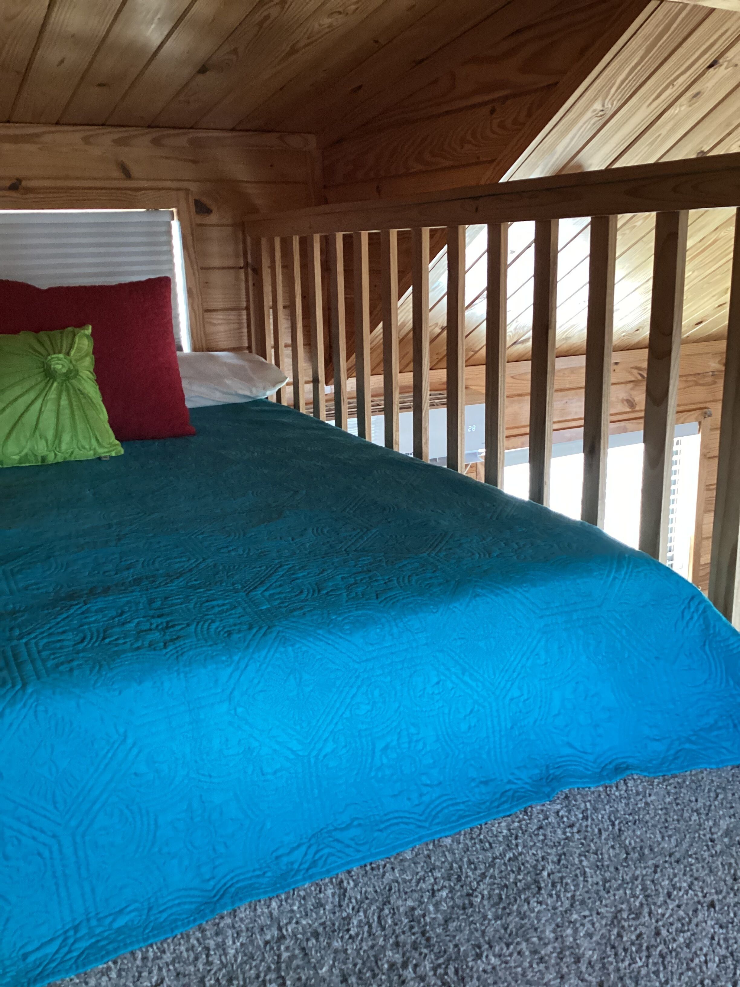 Interior de uma cabana de madeira com uma cama, um travesseiro vermelho e um travesseiro verde.