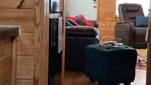 L’intérieur d’un chalet accueillant, avec un mur en bois, une porte, un canapé, un fauteuil et une petite table.
