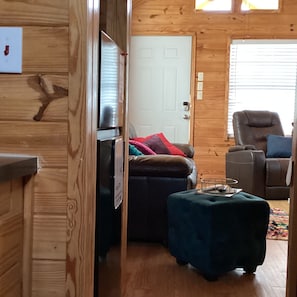 Indretning i en hyggelig hytte med trævæg, en dør, en sofa, en lænestol og et lille bord.