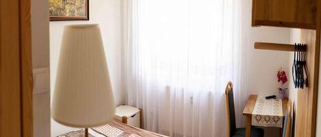A bedroom with a bed, a chair, a table with a lamp, and a painting on the wall.