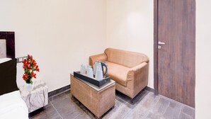 Een hotelkamer met een nachtkastje van marmer, een beige bank, een klein bijzettafeltje, een vaas met rode bloemen en een houten deur.