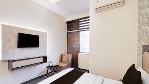Een moderne hotelkamer met een bed, een flatscreen-televisie aan de muur, een klein tafeltje met een dienblad, een stoel en een airconditioning.