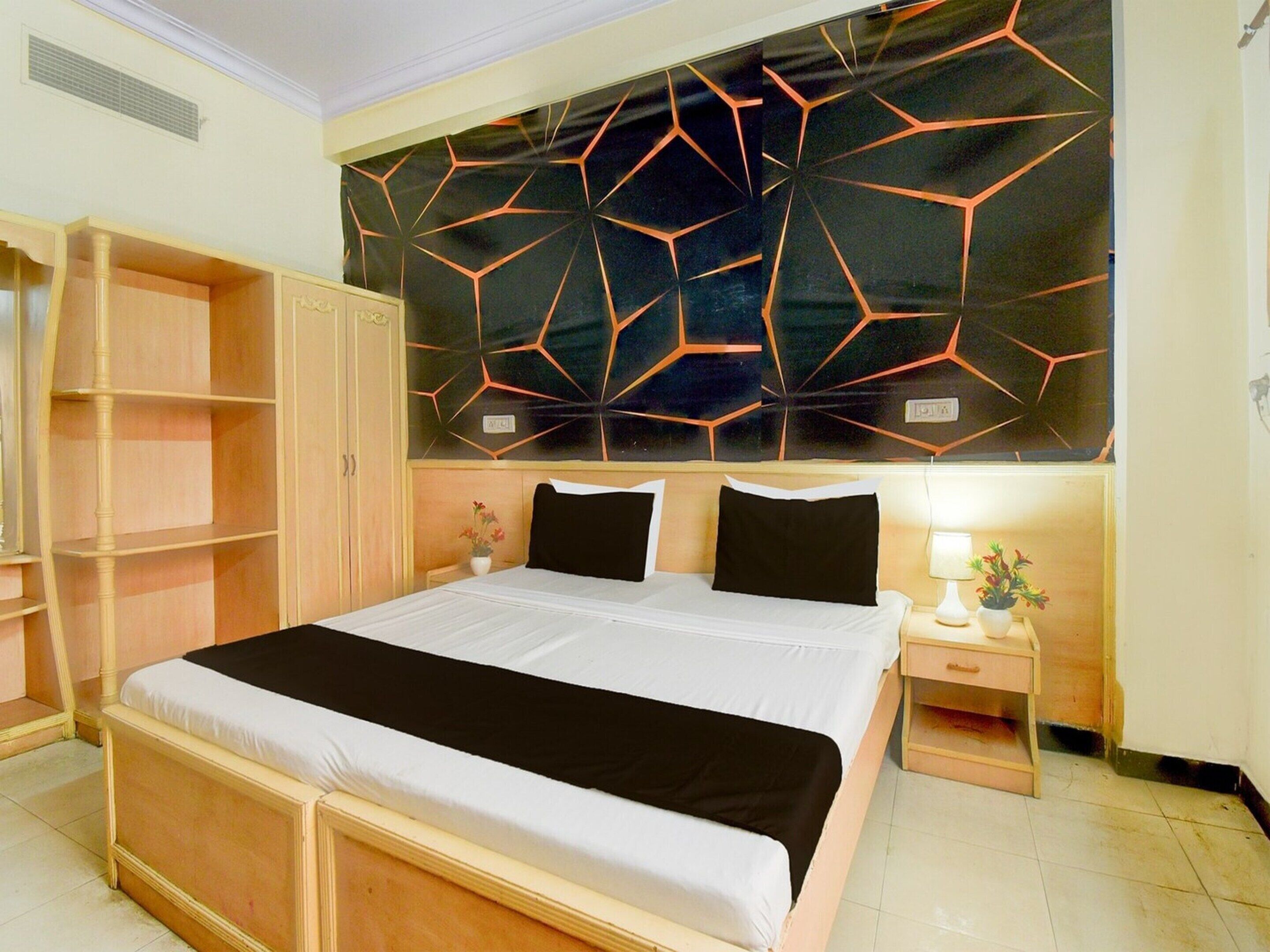 Un dormitorio con una cama, una mesita de noche, un armario de madera y una pared con estampado geométrico.