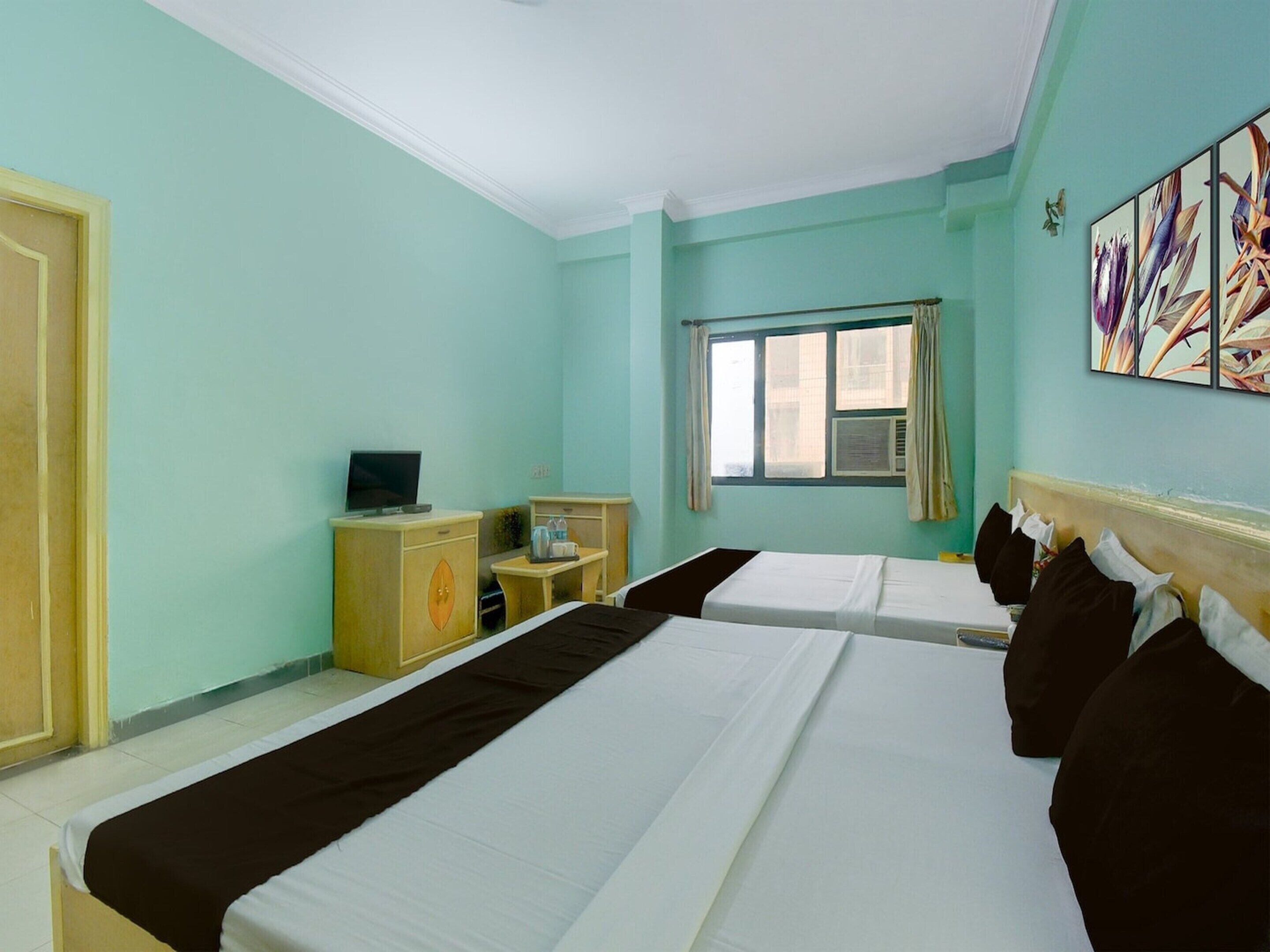 A hotel room with two beds, a television, a desk, and a window with curtains.