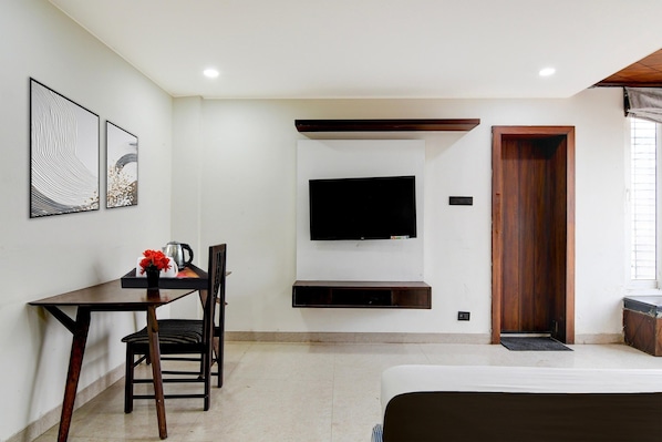 A hotel room with a bed, a desk with a chair, a TV mounted on the wall, and a wooden door.
