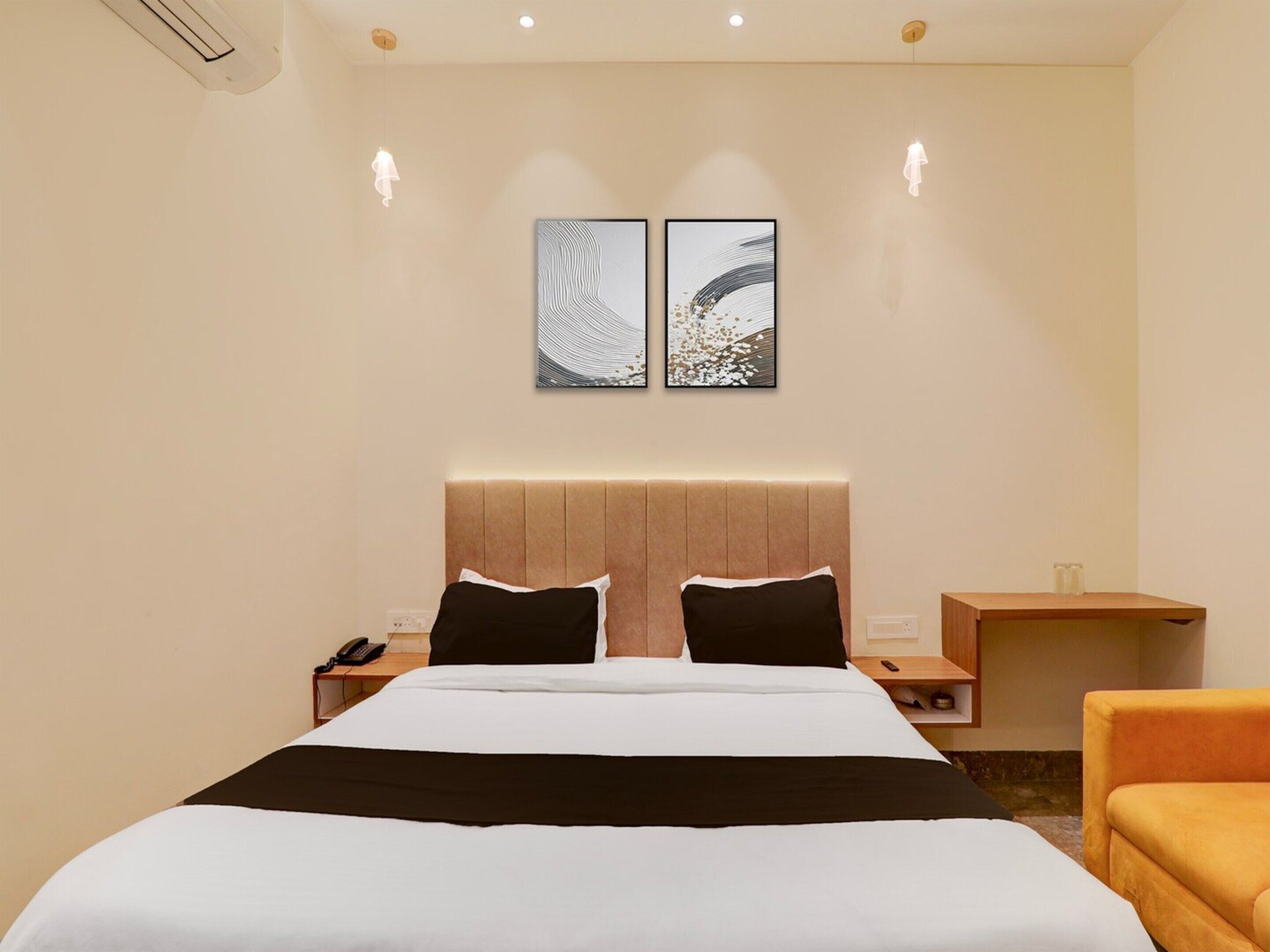 A hotel room with a large bed, two bedside tables, a nightstand, a chair, and two wall-mounted artworks.