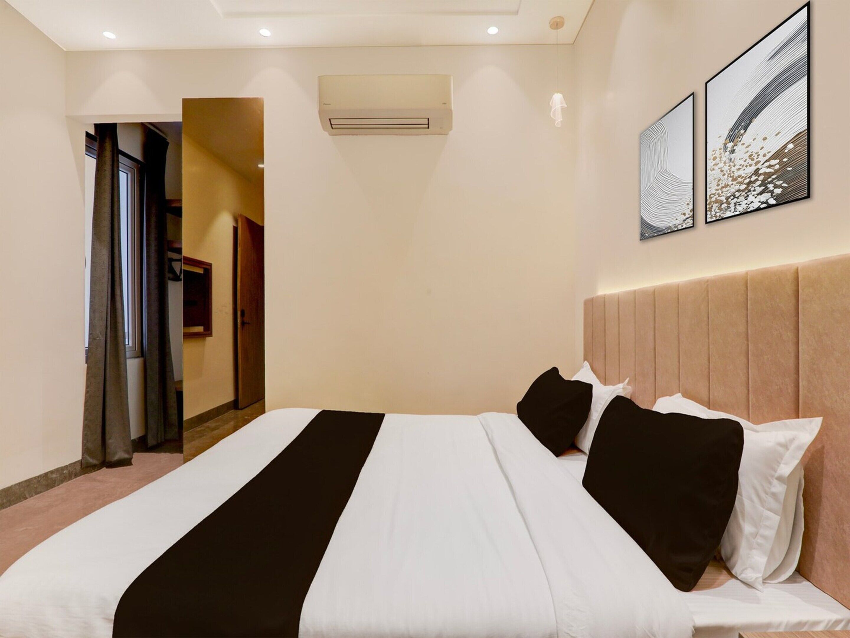 Una habitación de hotel con una cama, una puerta, un equipo de aire acondicionado y dos obras de arte colgadas en la pared.