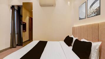 Una habitación de hotel con una cama, una puerta, un equipo de aire acondicionado y dos obras de arte colgadas en la pared.