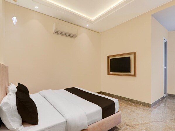 A hotel room with a bed, an air conditioning unit, a framed picture on the wall, and a door leading to another room.