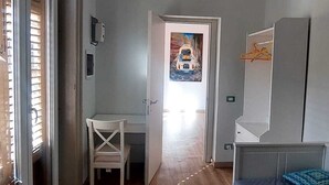 Une chambre à coucher avec un lit, un bureau et une chaise. Une porte donne accès à une autre pièce.