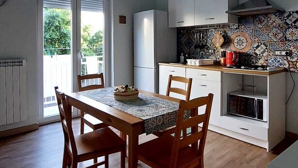 Un coin repas avec une table et des chaises en bois, une cuisine avec des meubles blancs et un dosseret carrelé, et un luminaire au plafond.