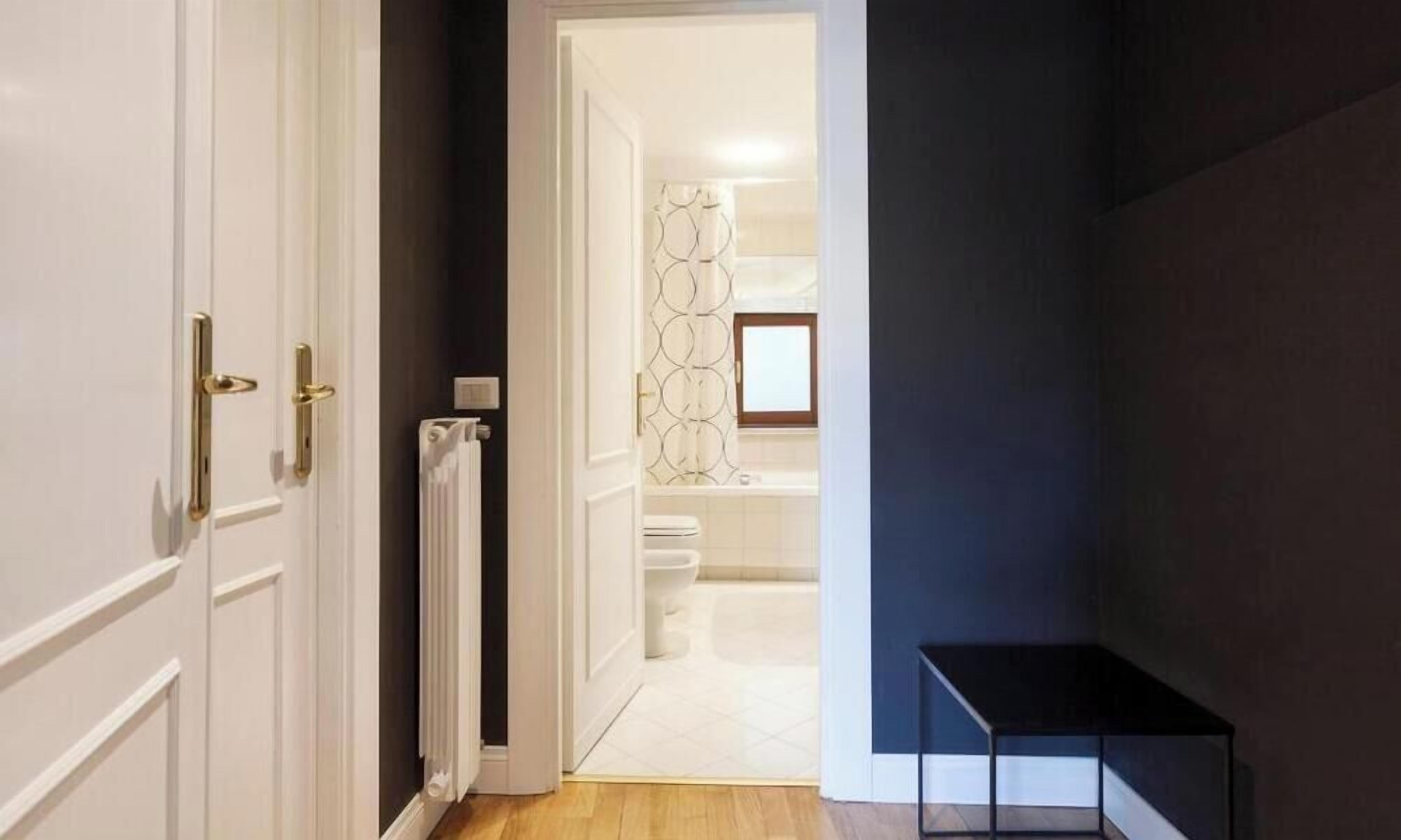 Ein Flur, der zu einem Badezimmer mit Toilette, Heizkörper und einer waschraumtypischen Duschvorhangs weist.