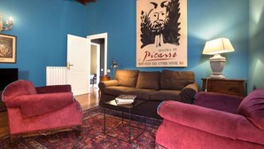 Ein Wohnzimmer mit blauer Wand, einem braunen Sofa, zwei roten Sesseln, einem gemusterten Teppich, einem gerahmten Kunstwerk und einer Lampe.