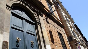 Ein Gebäude mit einer großen, dunkelblauen Tür, zwei Messinggriffen und einem kleinen Fenster mit einem Metallgitter.