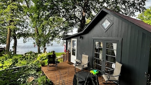 A wooden cabin with a deck, outdoor seating, and a view of a lake. - Spring-Fed Cabin w/ Waterfall & Lake Access, Kayaks & Fishing - Cabin 6 (South Haven)