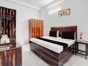 Ein modernes Hotelzimmer mit einem Holzschrank, einem Bett mit dunklem Kopfteil, einem Nachttisch mit einer Vase und Kunstwerken an der Wand.
