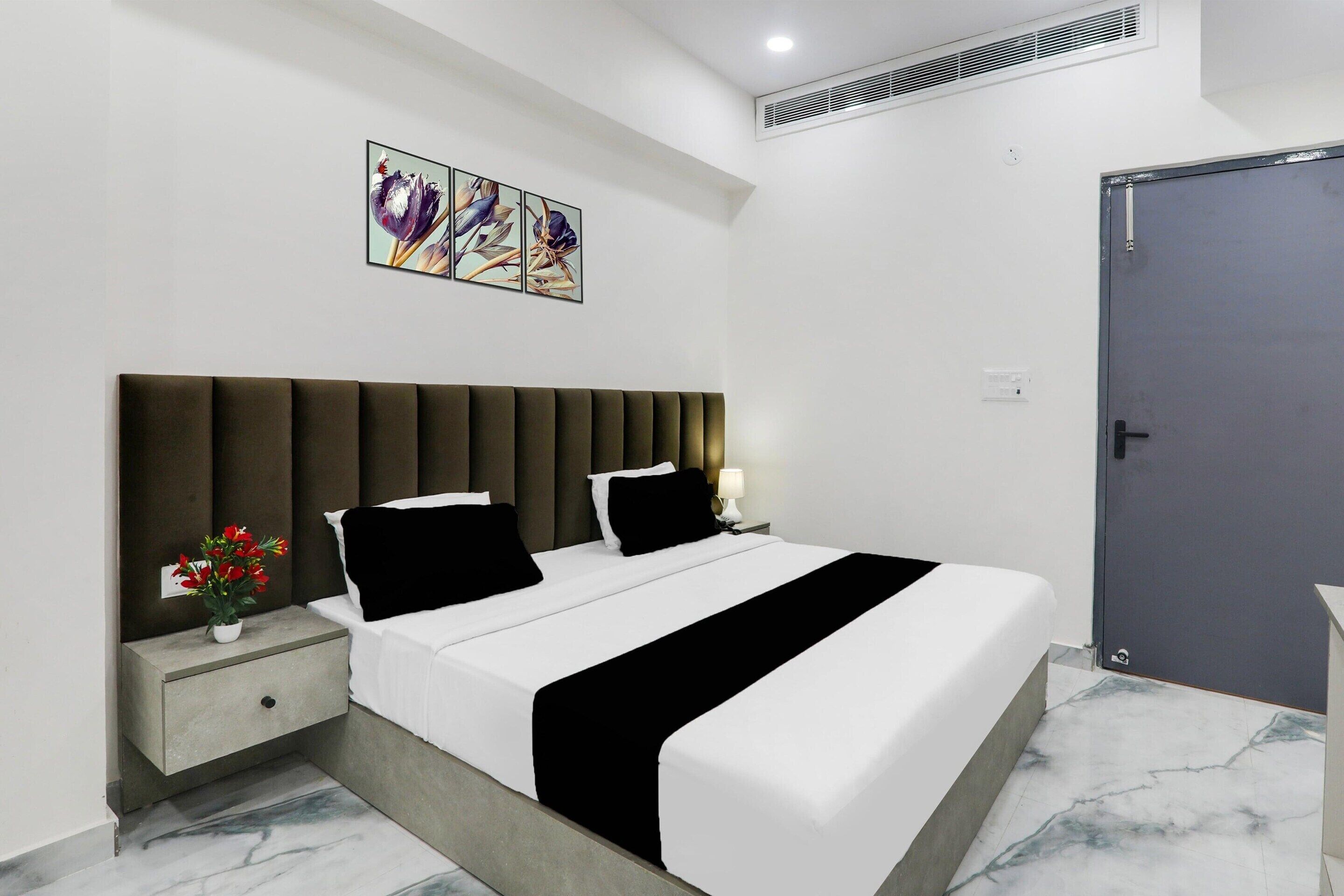 Une chambre d’hôtel moderne avec un grand lit, une table de chevet ornée d’un vase de fleurs, une porte et une œuvre d’art accrochée au mur.