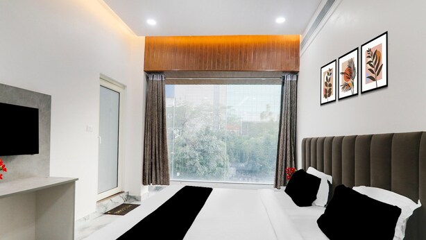 Habitación de hotel moderna con una cama grande, un televisor de pantalla plana, una ventana con cortinas y cuadros en la pared.