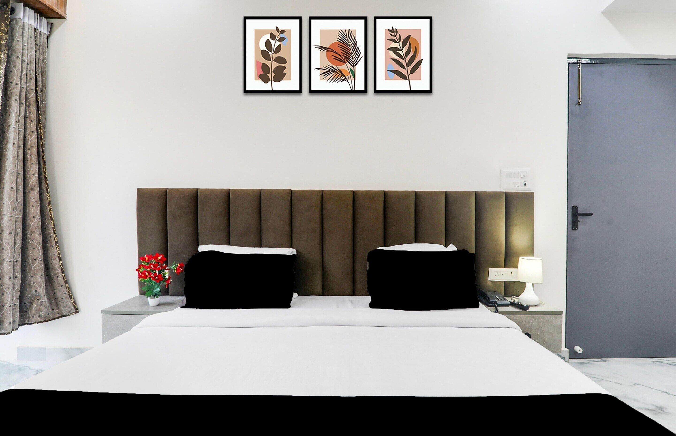 Una habitación de hotel con una cama grande, dos mesitas de noche, una mesita auxiliar, una puerta y tres cuadros enmarcados en la pared.