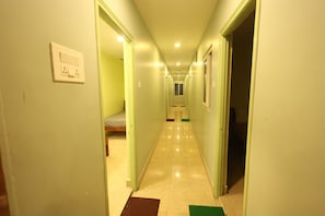 A narrow hallway with a bed at the end, a door on the right, and a light switch on the left.