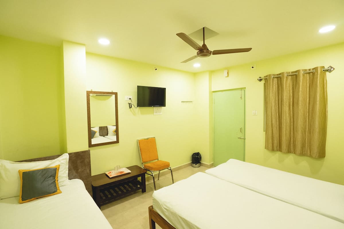A hotel room with two beds, a chair, a television, a ceiling fan, and a door.
