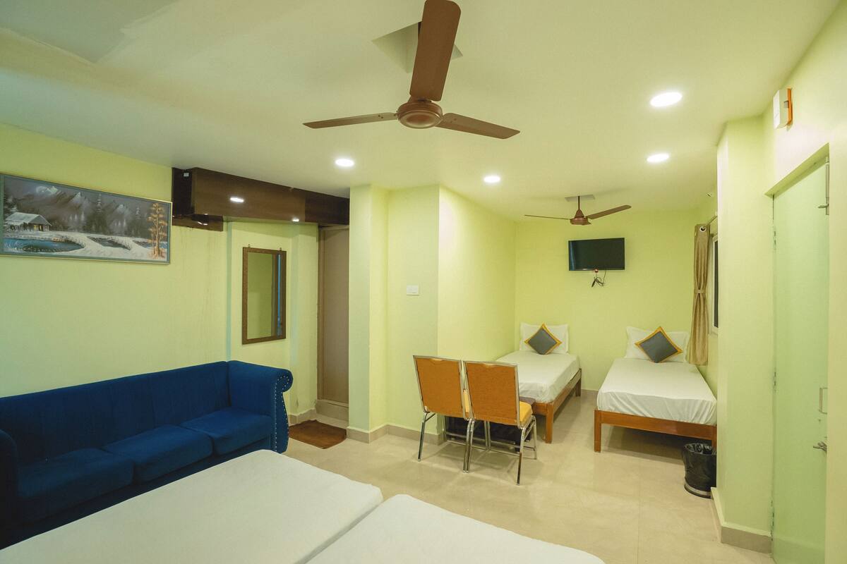 A hotel room with two beds, a blue sofa, a ceiling fan, a TV, and a painting on the wall.