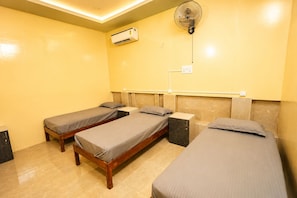 A room with three single beds, a wall-mounted air conditioner, and a ceiling fan.