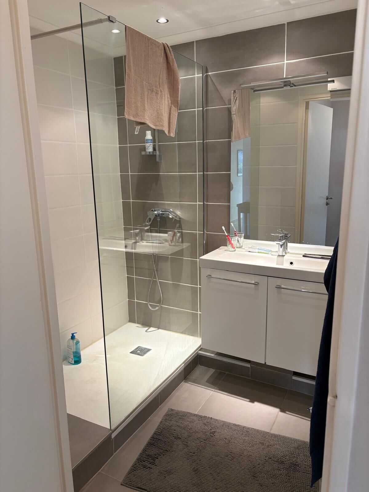 Een moderne badkamer met een glazen douchecabine, een wastafel met spiegel en een handdoek aan de muur.